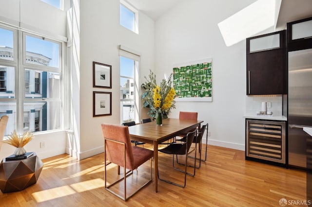 dining room with beverage cooler, light hardwood / wood-style floors, and a high ceiling