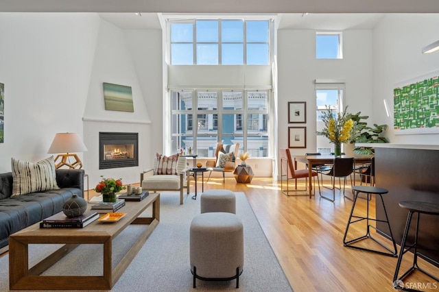 living room with light hardwood / wood-style flooring, a large fireplace, and a high ceiling