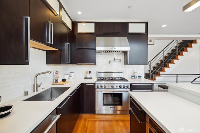 kitchen featuring dark brown cabinetry, wall chimney exhaust hood, sink, light hardwood / wood-style flooring, and stainless steel appliances