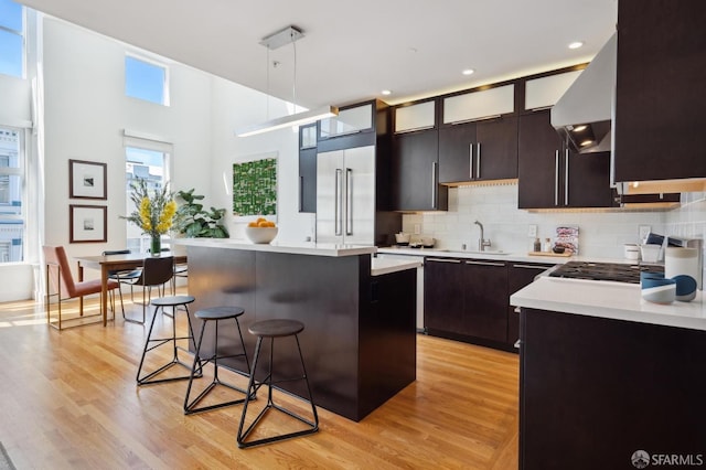 kitchen with sink, a breakfast bar, built in refrigerator, hanging light fixtures, and a center island