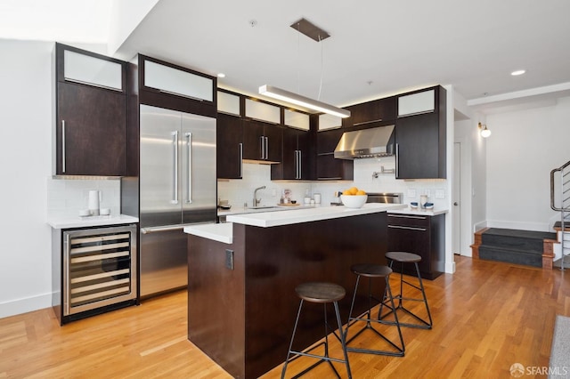 kitchen with stainless steel built in refrigerator, a breakfast bar, a center island, beverage cooler, and range hood