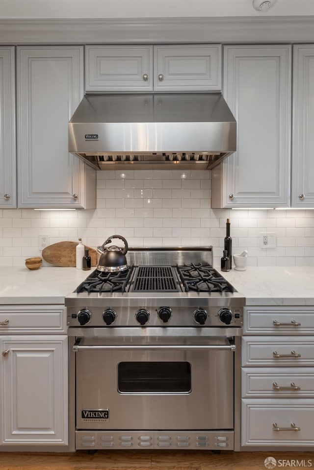 kitchen featuring premium stove, decorative backsplash, light stone countertops, and under cabinet range hood