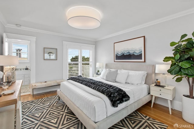 bedroom with ornamental molding, light wood-style flooring, and ensuite bath