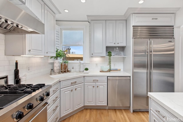 kitchen with appliances with stainless steel finishes, white cabinetry, light wood finished floors, and ventilation hood