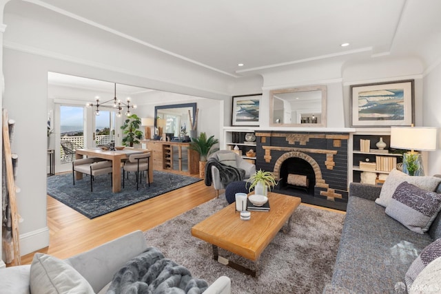 living area with a fireplace, ornamental molding, a notable chandelier, and wood finished floors