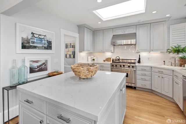 kitchen featuring a skylight, a center island, stainless steel appliances, under cabinet range hood, and a sink