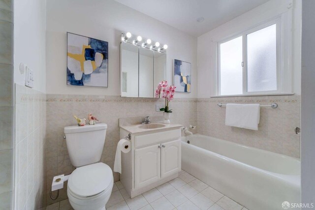 bathroom with tile patterned flooring, a bathing tub, toilet, vanity, and tile walls