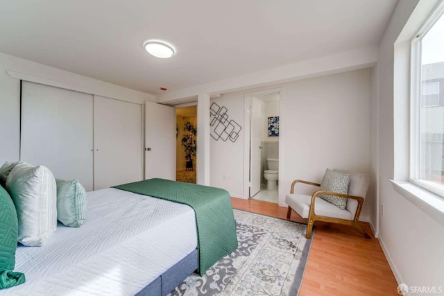 bedroom with light wood finished floors, a closet, ensuite bath, and baseboards