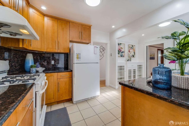 kitchen with white appliances, decorative backsplash, brown cabinets, under cabinet range hood, and light tile patterned flooring