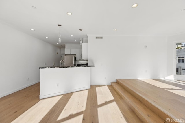 kitchen with sink, light hardwood / wood-style flooring, stainless steel refrigerator, white cabinets, and decorative light fixtures