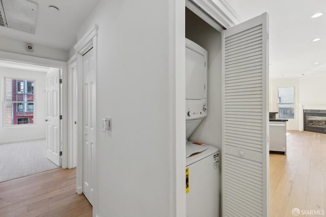 clothes washing area with a wealth of natural light, light wood-type flooring, and stacked washing maching and dryer