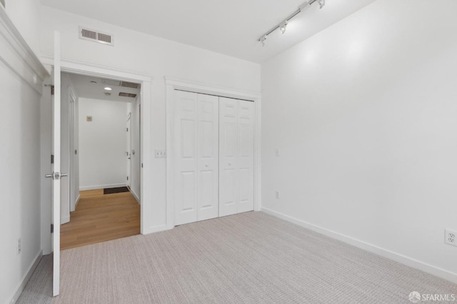 unfurnished bedroom featuring track lighting, light colored carpet, and a closet