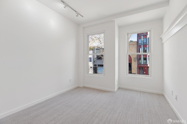 spare room featuring rail lighting and light colored carpet