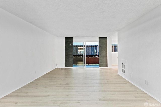 spare room with light wood-type flooring, floor to ceiling windows, and a textured ceiling