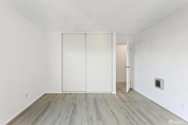 unfurnished bedroom with heating unit, a closet, a textured ceiling, light wood-type flooring, and baseboards