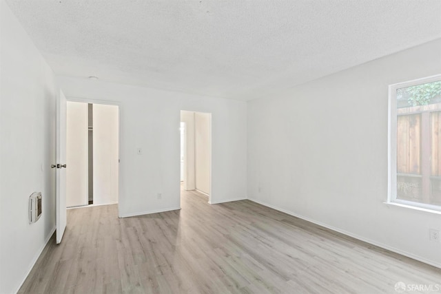 unfurnished bedroom with a textured ceiling, light wood finished floors, and baseboards