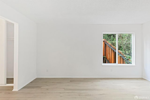 spare room featuring a textured ceiling, light wood-type flooring, and baseboards