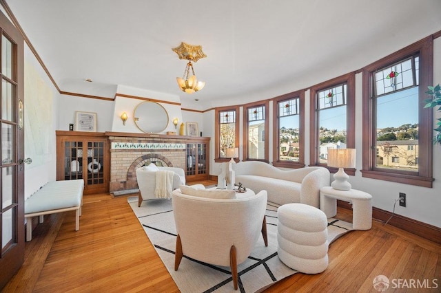 living room with a chandelier, light wood-type flooring, a brick fireplace, and crown molding