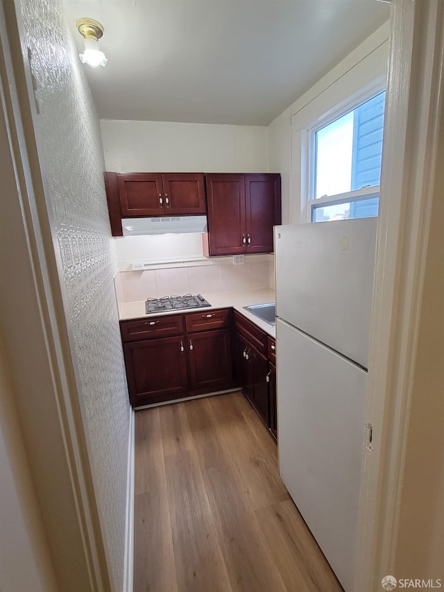 kitchen with decorative backsplash, stainless steel gas cooktop, light hardwood / wood-style flooring, sink, and white refrigerator