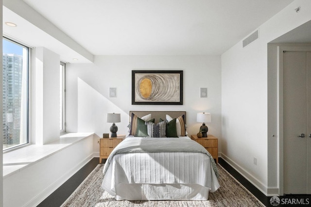 bedroom with a city view, recessed lighting, visible vents, wood finished floors, and baseboards