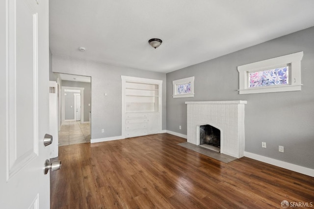 unfurnished living room with baseboards, wood finished floors, and a fireplace