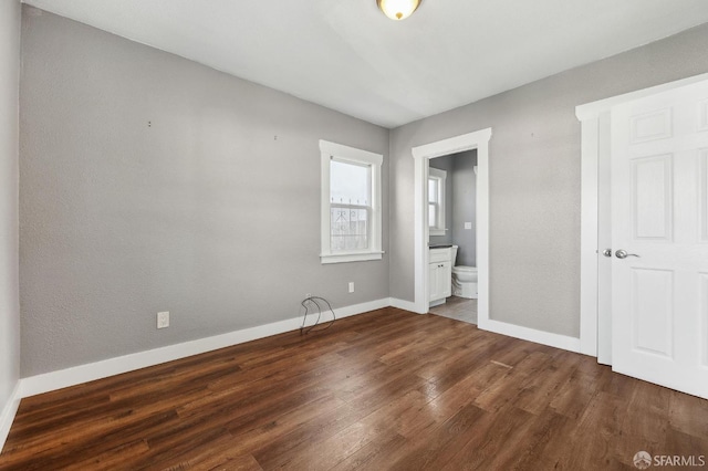 unfurnished bedroom featuring baseboards, ensuite bathroom, and dark wood-style floors