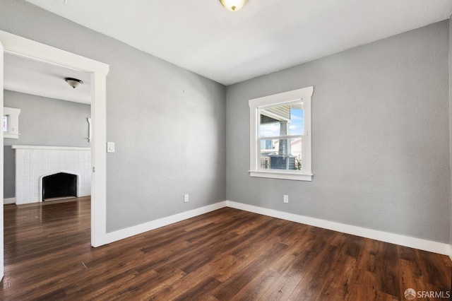 unfurnished room with baseboards, a fireplace, and dark wood finished floors
