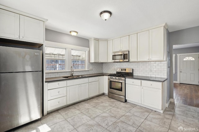 kitchen with backsplash, dark countertops, appliances with stainless steel finishes, and a sink
