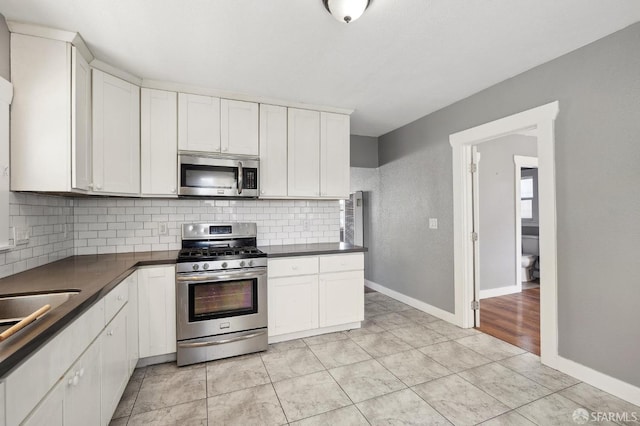 kitchen featuring dark countertops, tasteful backsplash, baseboards, stainless steel appliances, and white cabinetry