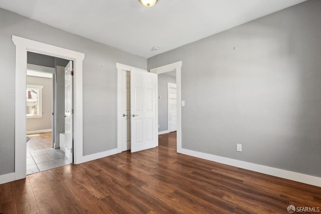 unfurnished bedroom with baseboards, ensuite bathroom, and dark wood-type flooring