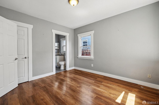 unfurnished bedroom with baseboards, ensuite bathroom, and wood finished floors