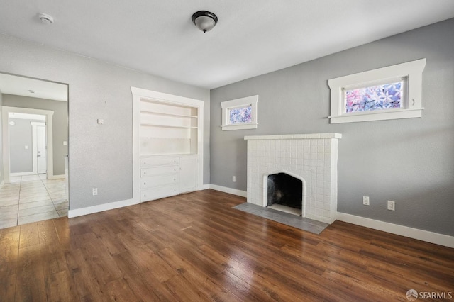 unfurnished living room with baseboards, built in shelves, wood finished floors, and a fireplace