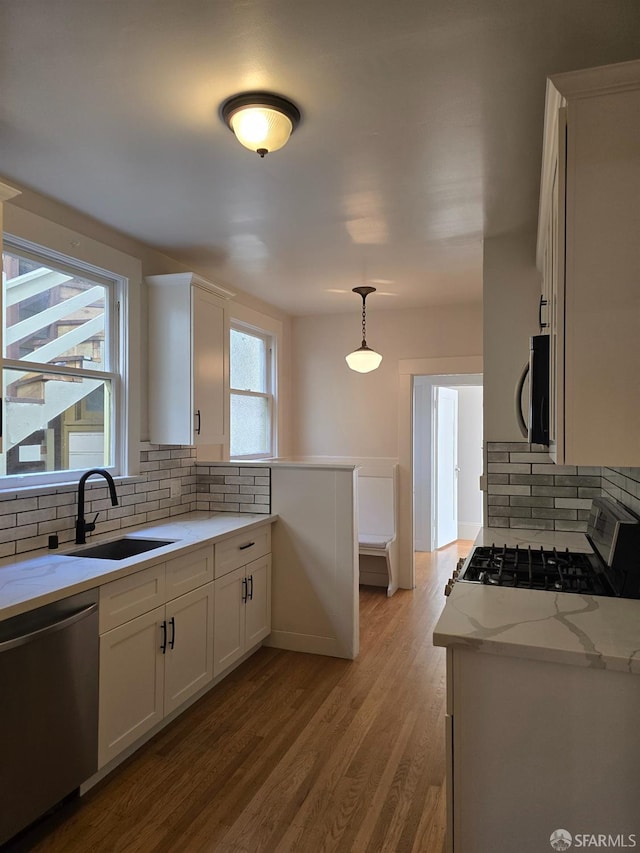 kitchen with sink, hanging light fixtures, stainless steel appliances, white cabinets, and light hardwood / wood-style flooring