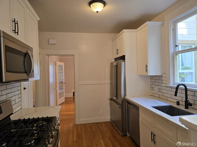 kitchen with appliances with stainless steel finishes, white cabinets, tasteful backsplash, and sink