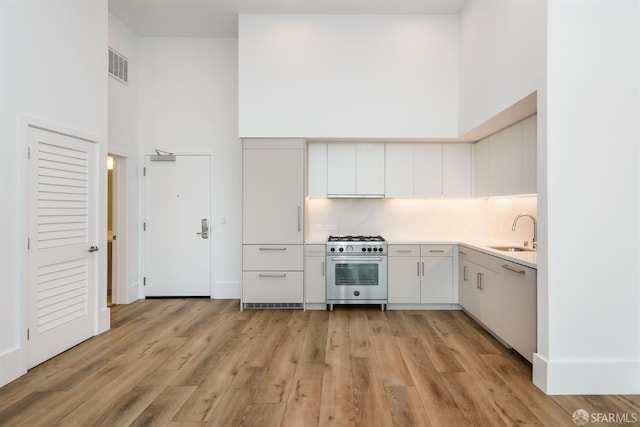 kitchen featuring light wood-style flooring, a high ceiling, a sink, visible vents, and high end stainless steel range oven