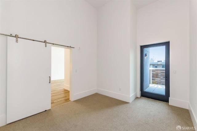 spare room featuring light carpet, a high ceiling, and baseboards