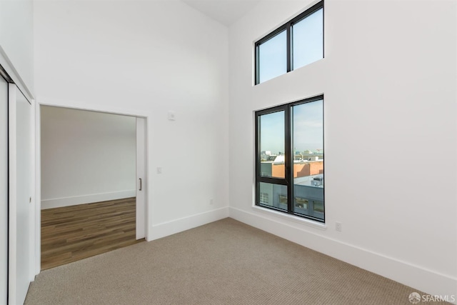 carpeted empty room featuring a high ceiling and baseboards