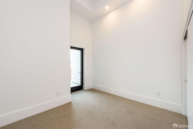 spare room with light carpet, recessed lighting, a towering ceiling, and baseboards