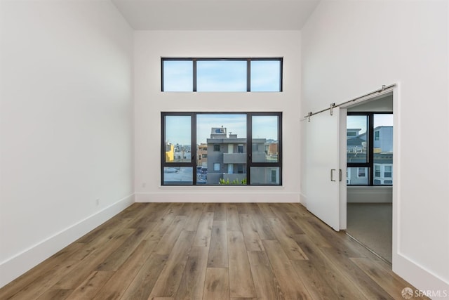 unfurnished room with a healthy amount of sunlight, a barn door, baseboards, and wood finished floors