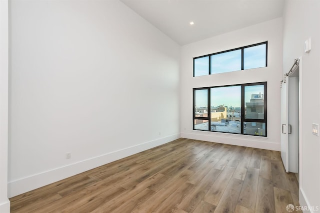 empty room with a barn door, a towering ceiling, light wood-style flooring, and baseboards