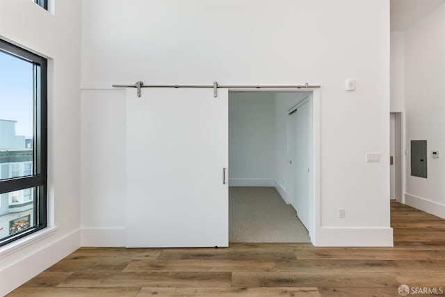 unfurnished room featuring a barn door, electric panel, baseboards, and wood finished floors