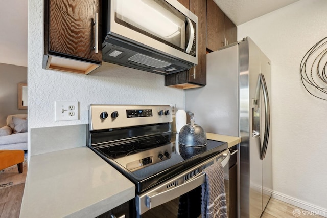 kitchen featuring stainless steel appliances, dark brown cabinets, and light wood-type flooring