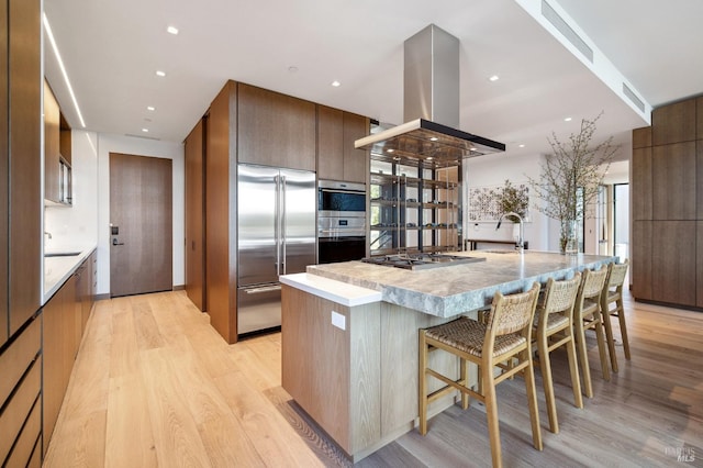kitchen featuring a kitchen breakfast bar, island exhaust hood, modern cabinets, appliances with stainless steel finishes, and light wood finished floors