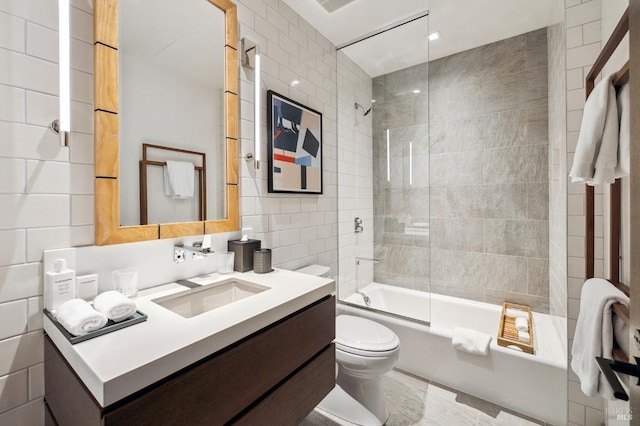 bathroom featuring toilet, bathing tub / shower combination, vanity, and tile walls