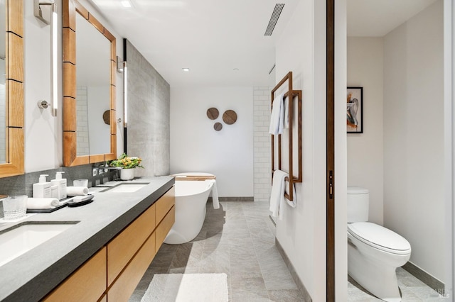 full bathroom featuring visible vents, toilet, a sink, a freestanding bath, and double vanity