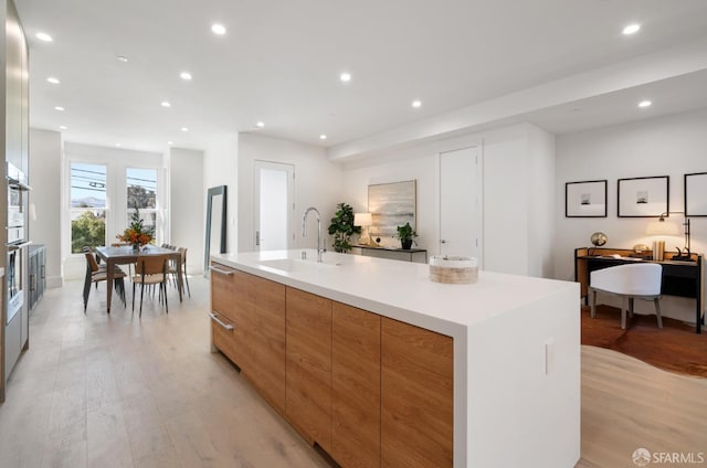 kitchen featuring sink, oven, a large island with sink, and light wood-type flooring