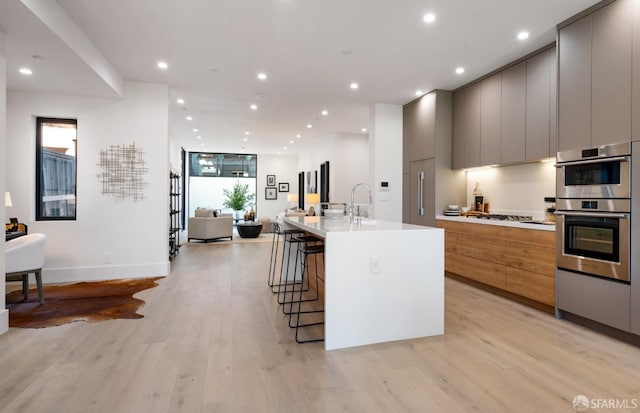 kitchen with a large island, light hardwood / wood-style flooring, a breakfast bar, gray cabinetry, and stainless steel double oven