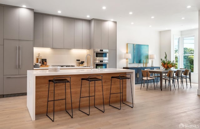 kitchen featuring gray cabinets, double oven, a spacious island, a kitchen bar, and light wood-type flooring