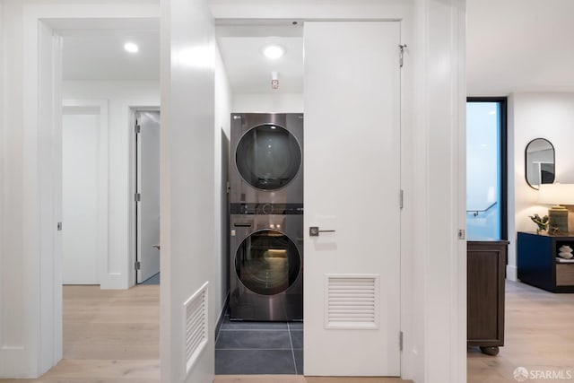 clothes washing area with stacked washer / drying machine and light wood-type flooring