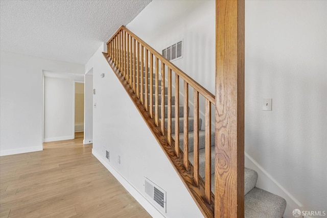 staircase featuring a textured ceiling and hardwood / wood-style flooring